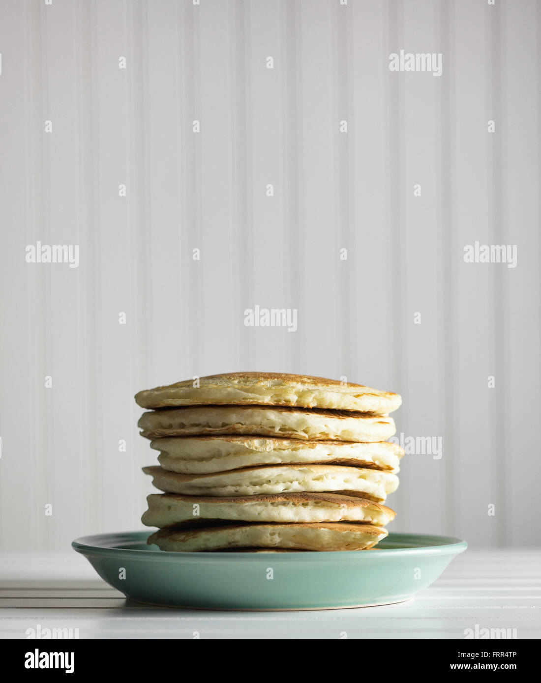 Hohe Stapel von Pfannkuchen auf einen blauen Teller vor einem weißen Hintergrund. Stockfoto