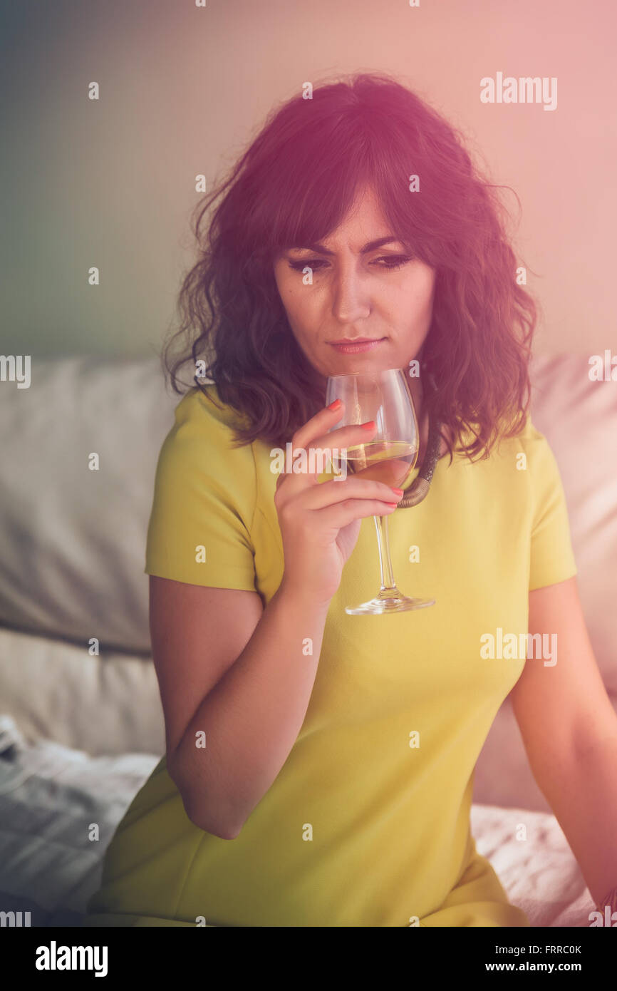 Erhöhte Ansicht einer nachdenklich nachdenklichen jungen Frau, die bei einem Glas Weißwein sitzt auf dem Sofa mit einem bunten Leuchteffekt Stockfoto