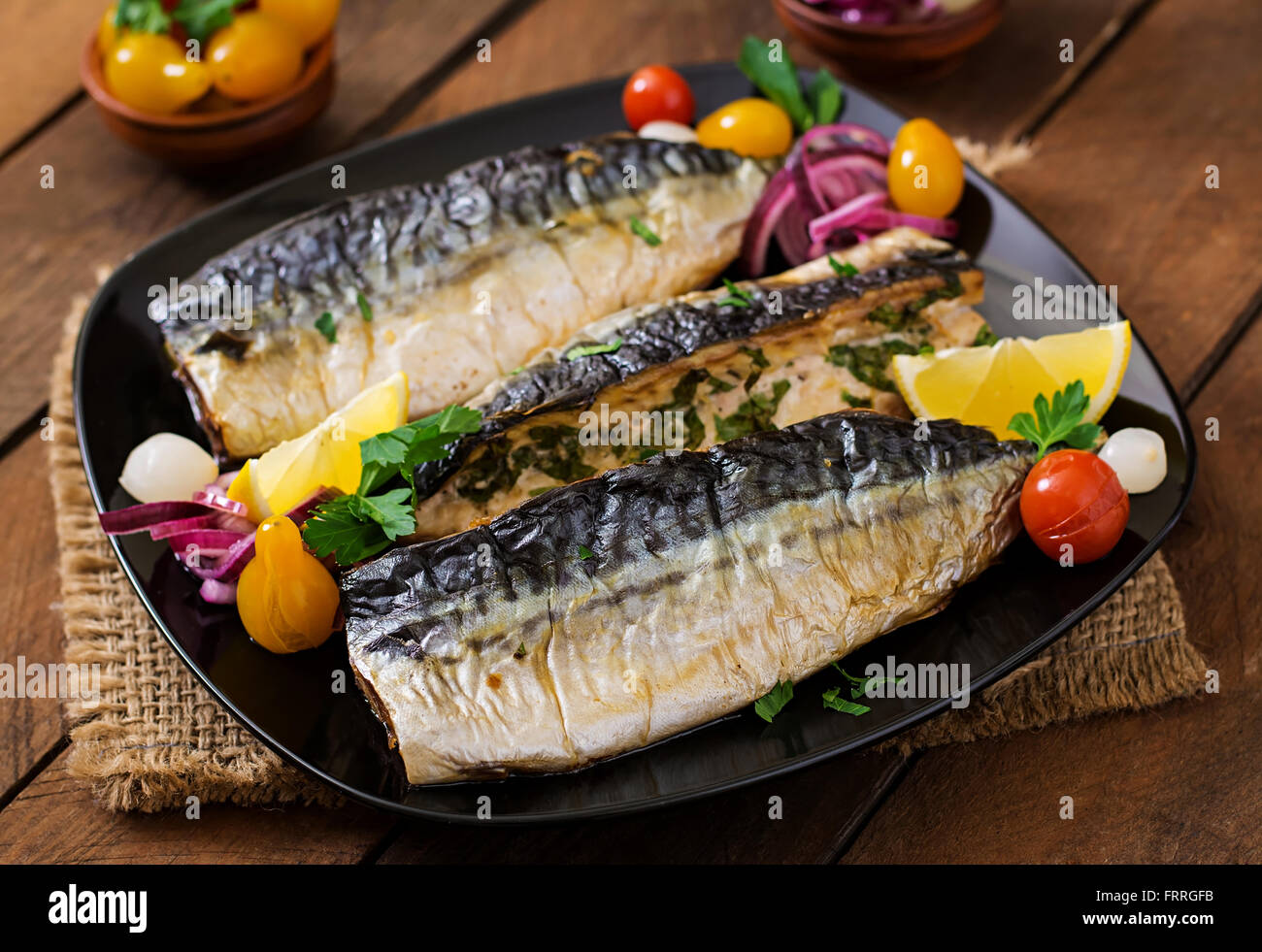 Gebackene Makrele mit Kräutern und garniert mit Zitrone und eingelegtem Gemüse Stockfoto