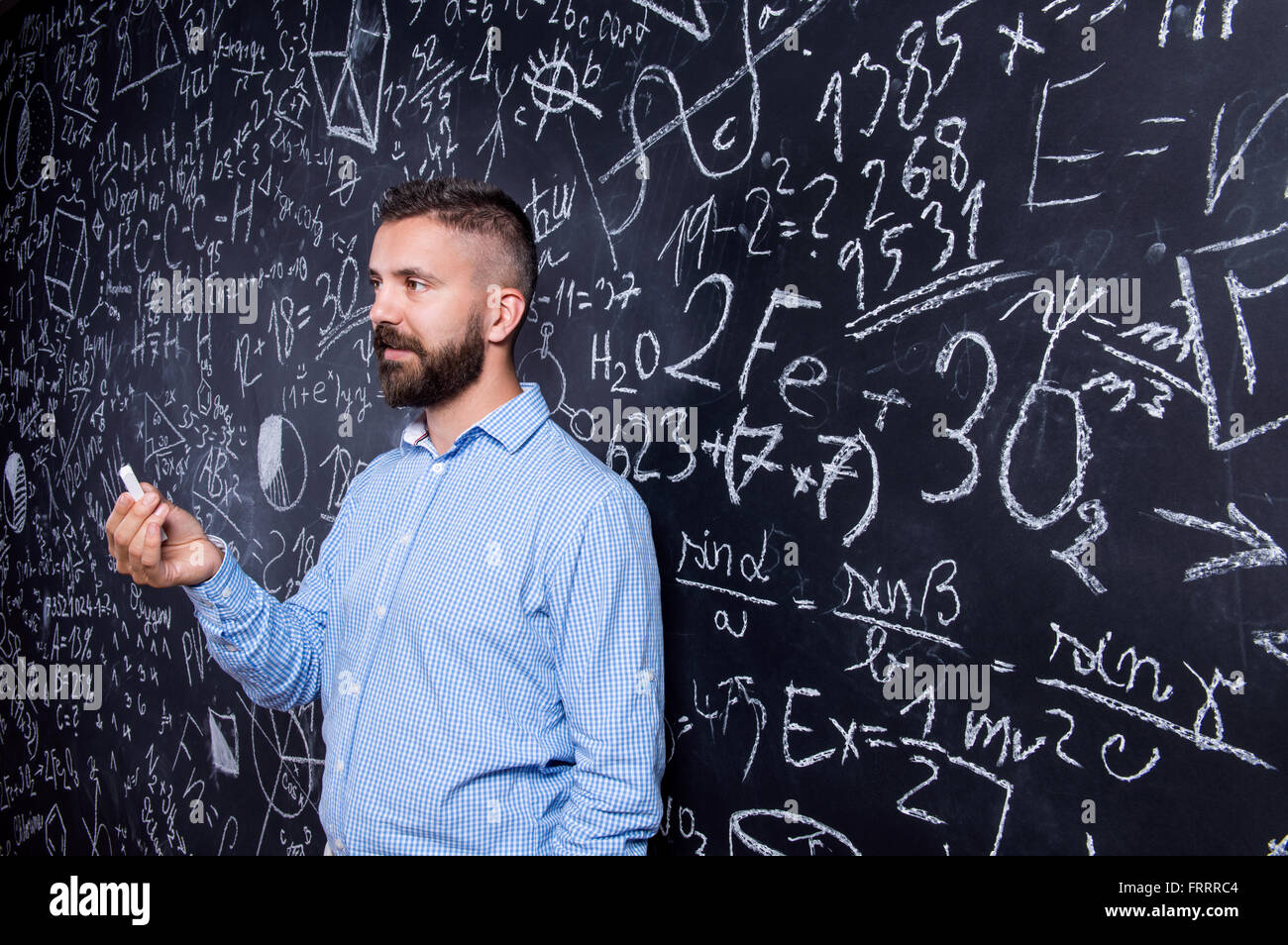 Hipster Lehrer gegen große Tafel mit mathematischen Symbolen Stockfoto