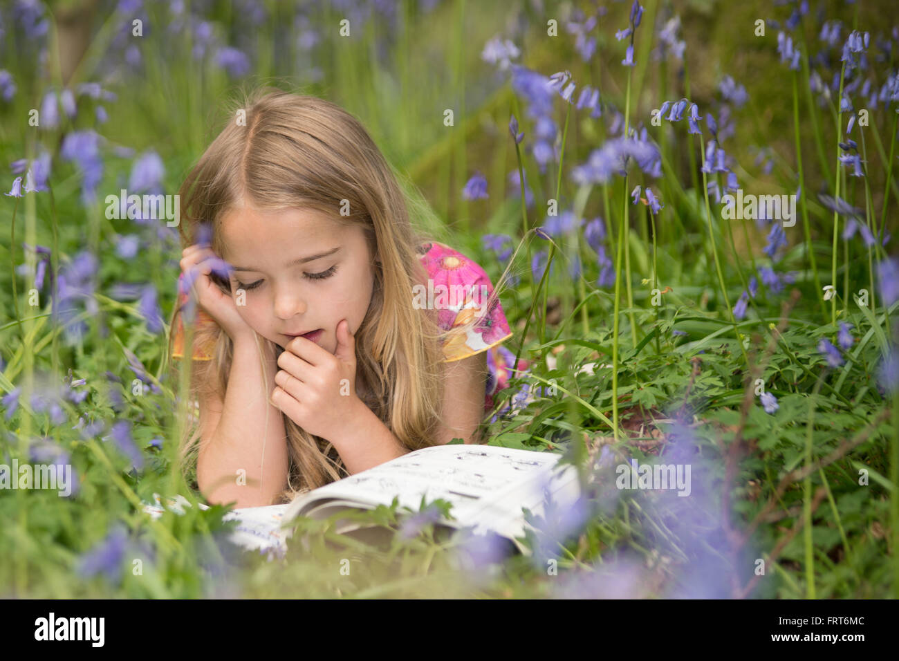 junge blonde kurzhaarige Mädchen liegen in einem Bett aus blauen Glocken Blumen ihr Buch zu lesen Stockfoto