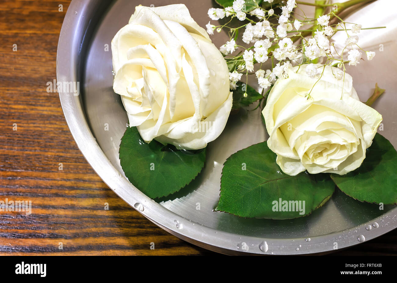 Auf der Oberfläche des Wassers im Behälter ist eine schöne weiße Rosen und kleinen weißen Blüten. Stockfoto