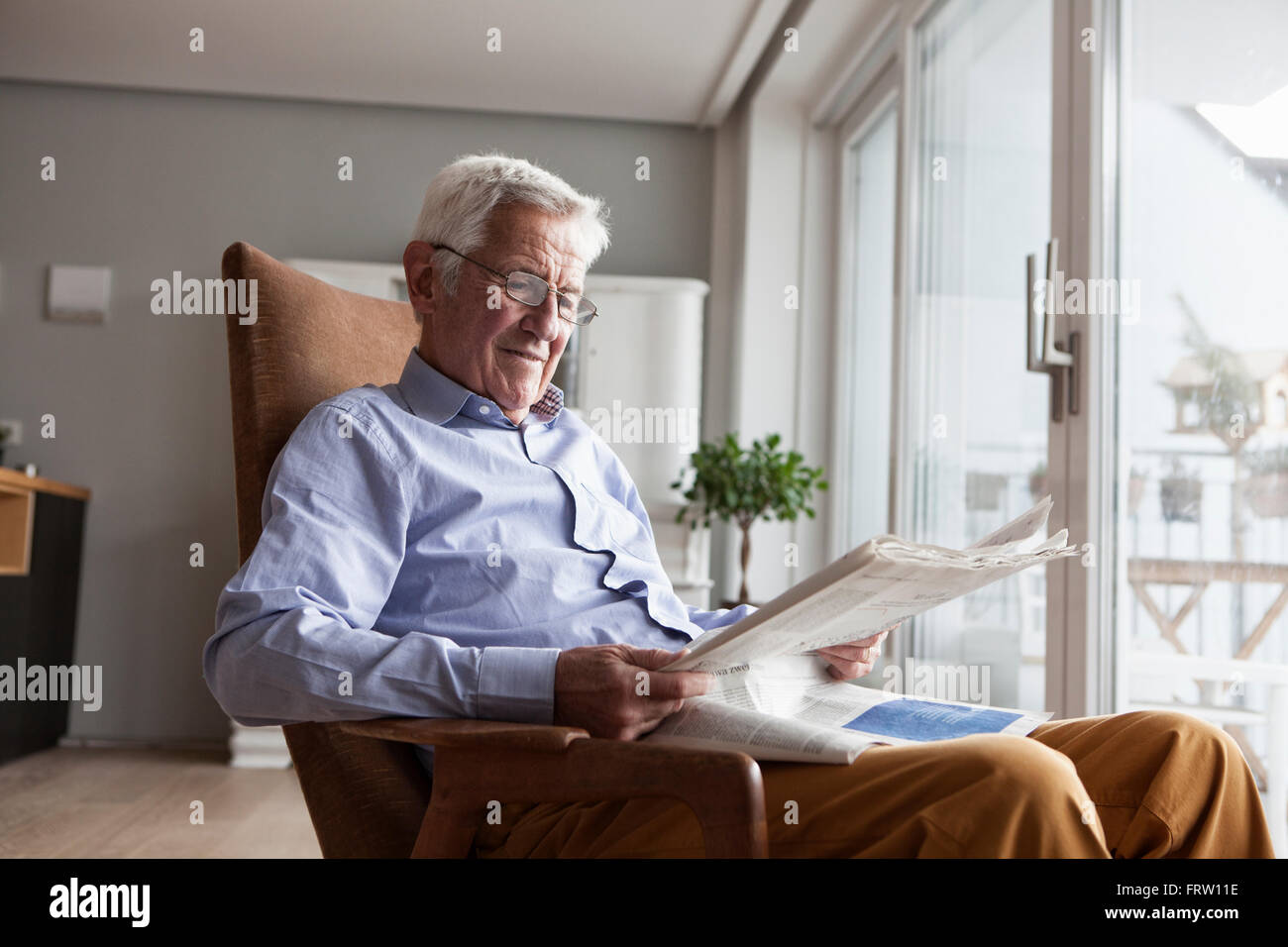 Porträt von senior Mann sitzt auf Sessel zu Hause lesen Zeitung Stockfoto