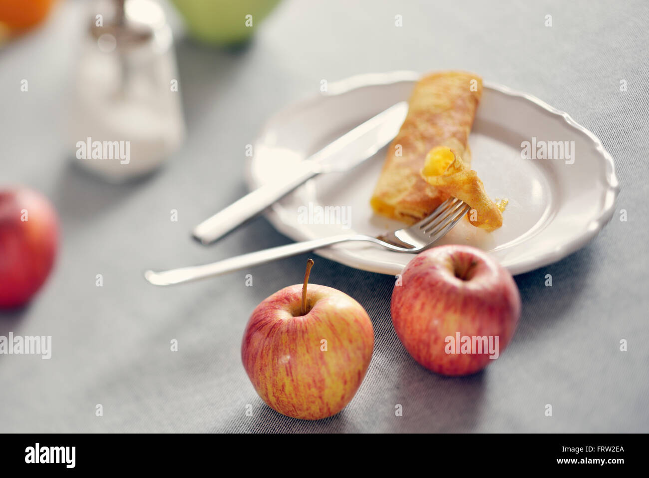 Gerollte Pfannkuchen auf Teller und Äpfel Stockfoto