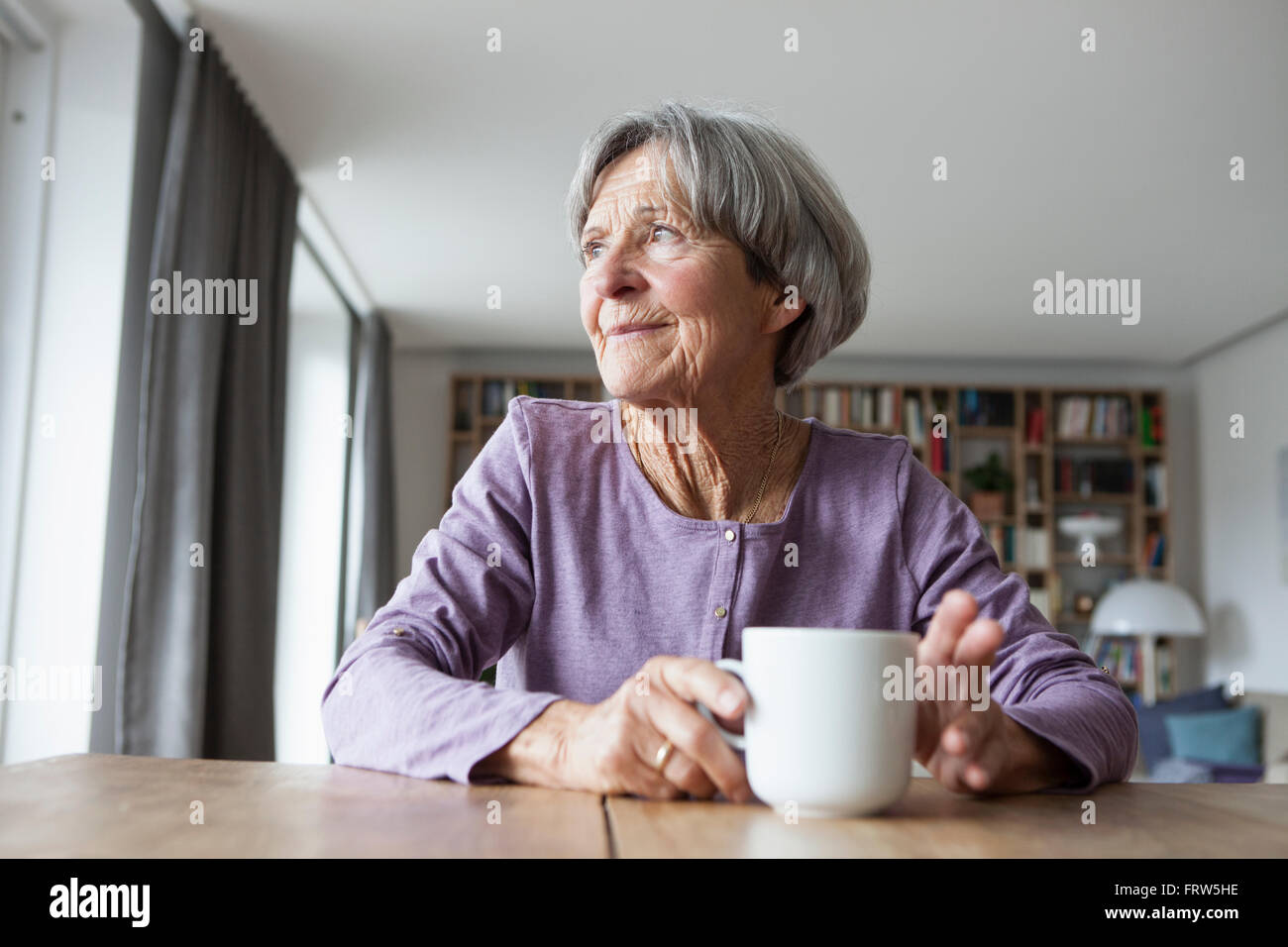 Porträt von senior Frau sitzt am Tisch mit Tasse Kaffee mit Blick durch Fenster Stockfoto