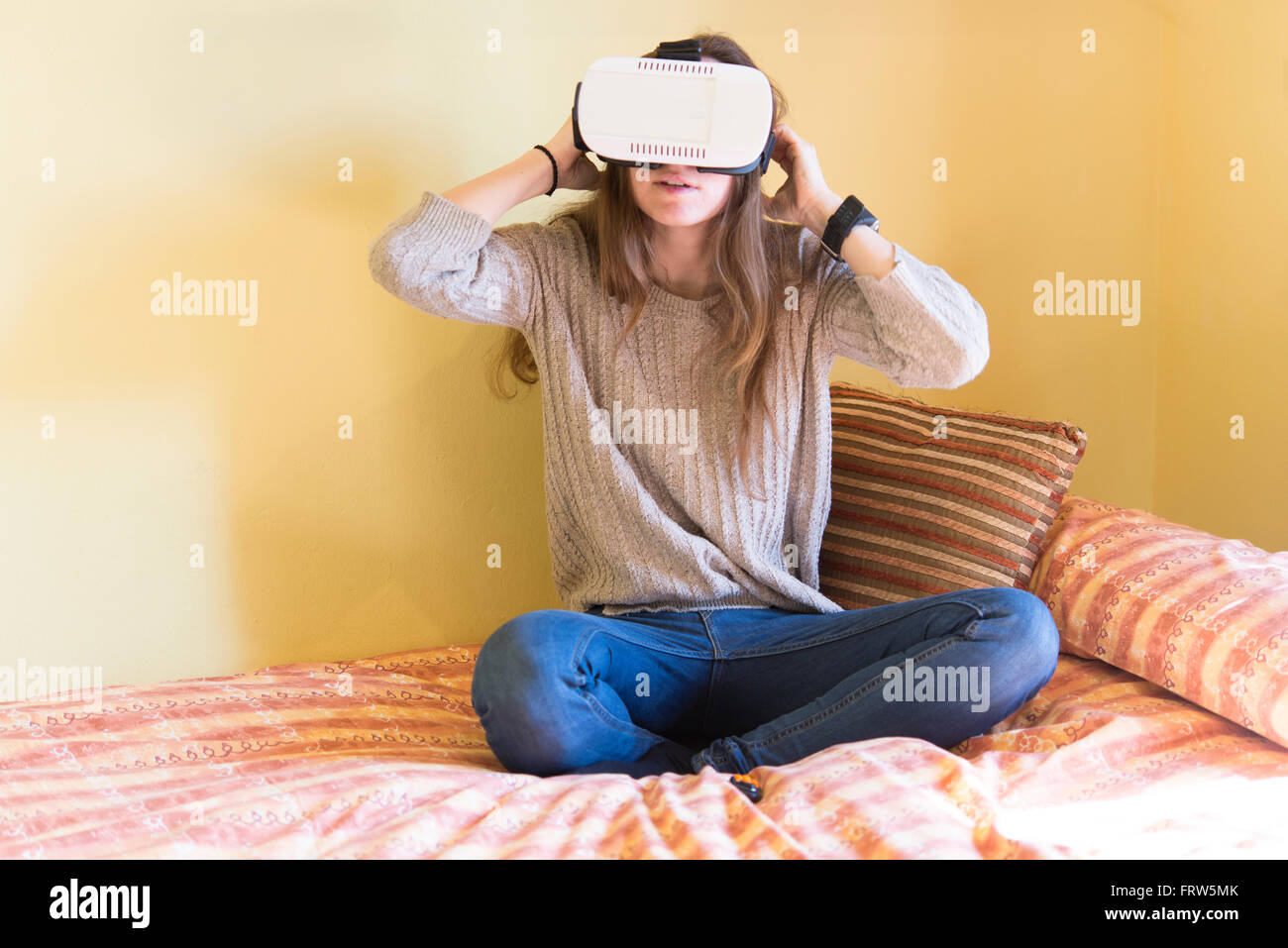 Junge Frau mit Virtual-Reality-Brille sitzt auf ihrem Bett zu Hause Stockfoto