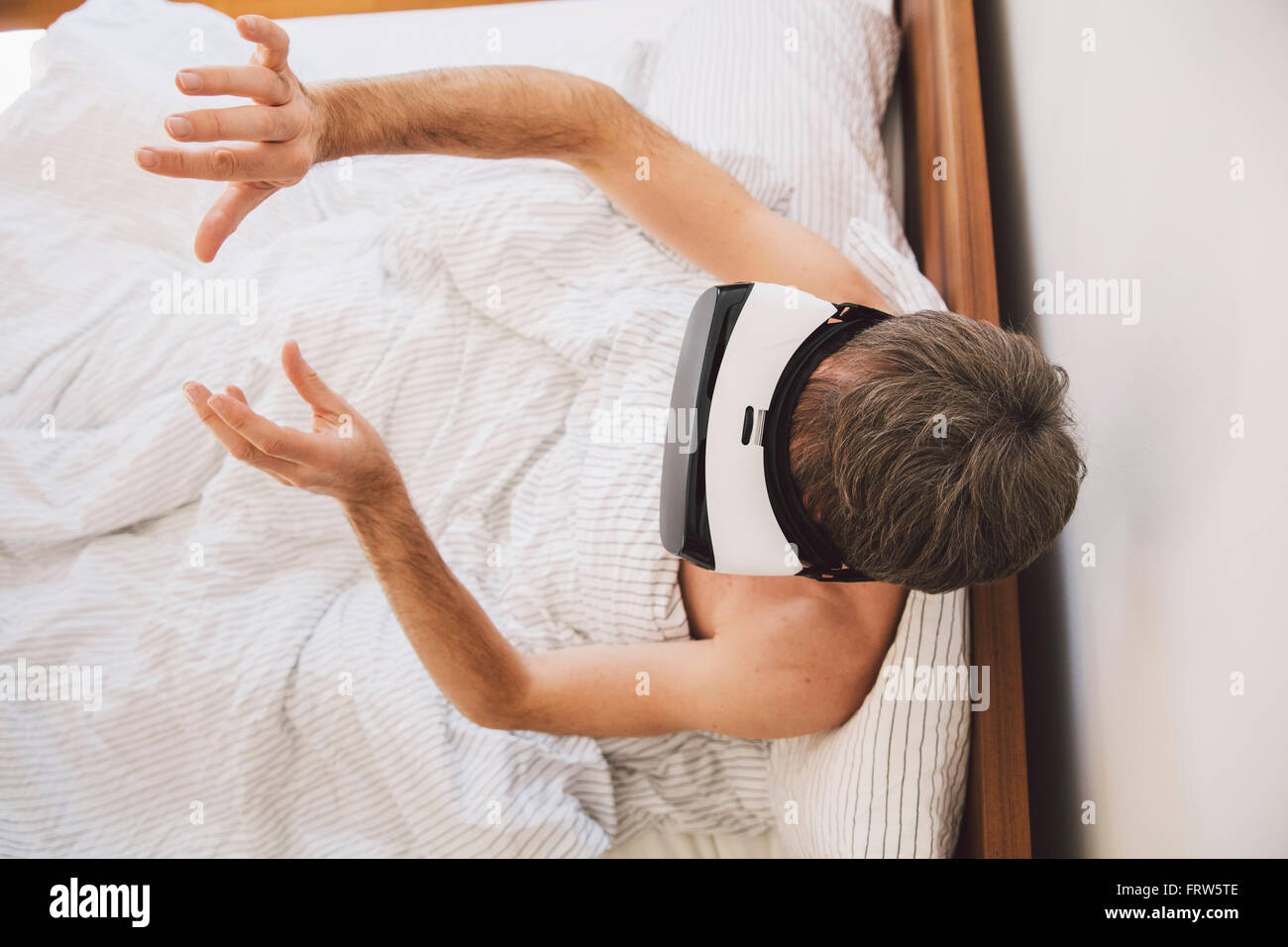 Mann im Bett mit virtual-Reality-Brille, bewegte seine Hände Stockfoto