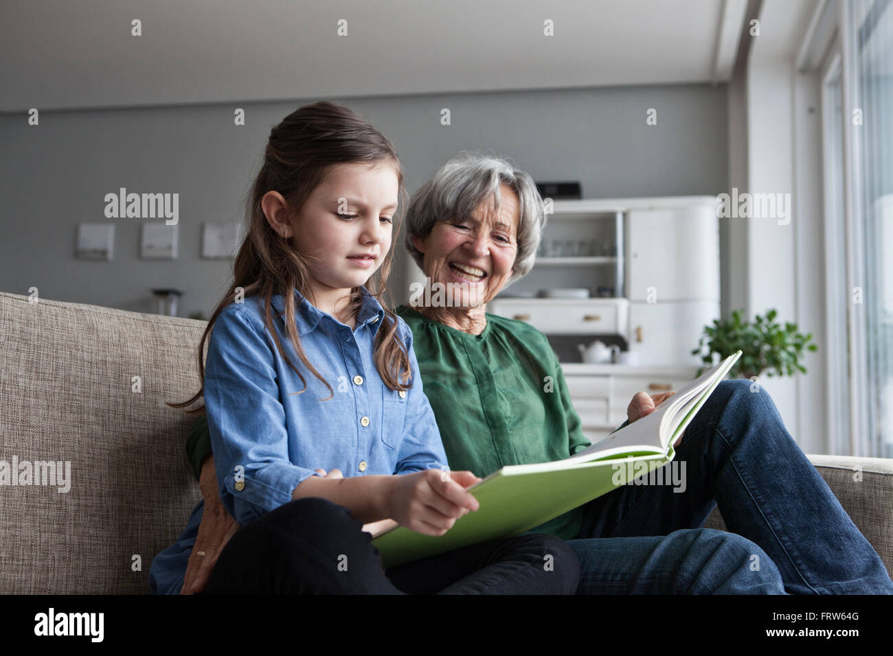Großmutter und Enkelin zusammen mit einem Buch auf der Couch sitzen Stockfoto