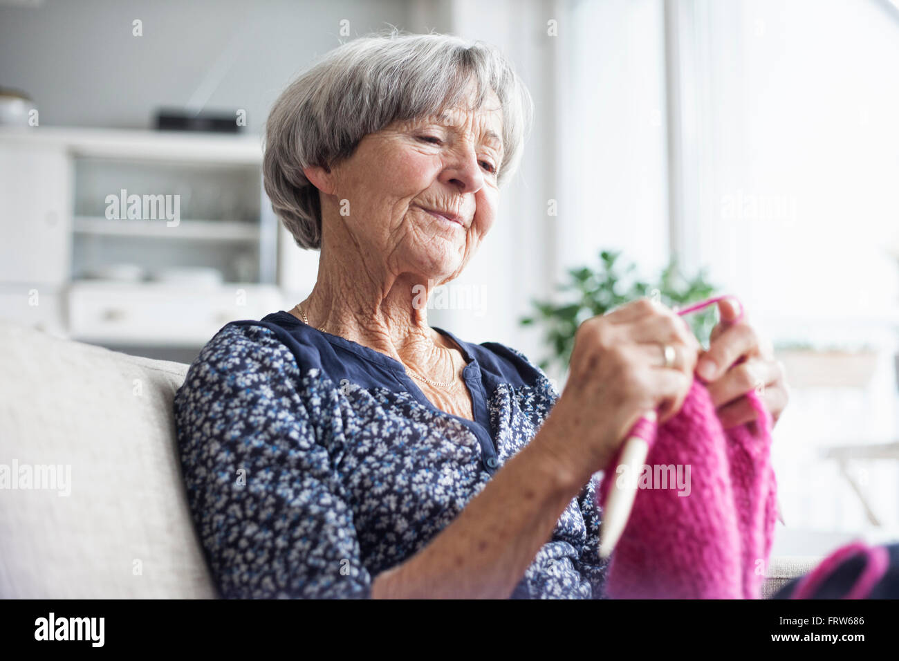 Porträt der strickenden senior Frau sitzt auf der Couch zu Hause Stockfoto