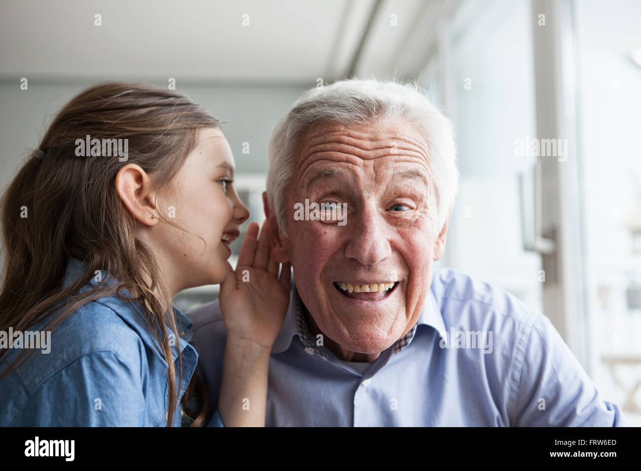 Enkelin Flüstern etwas in das Ohr ihres Großvaters Stockfoto