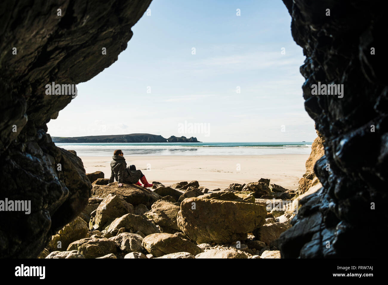 Frankreich, Bretagne, Finistere, Halbinsel Crozon, Frau sitzt am Strand von Felsenhöhle gesehen Stockfoto