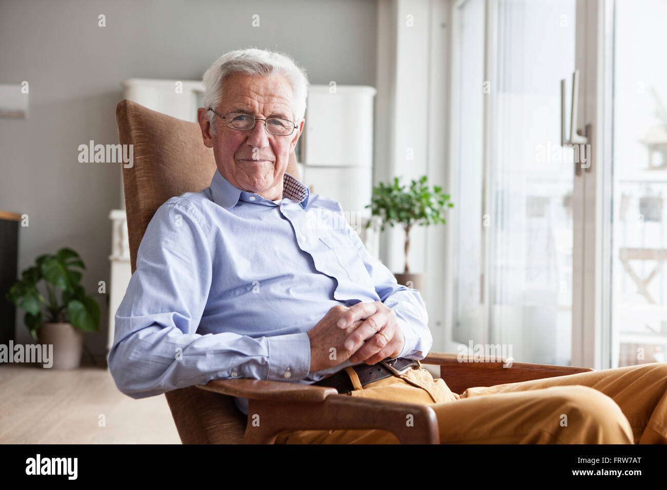 Porträt von lächelnden senior Mann sitzt auf Sessel zu Hause Stockfoto