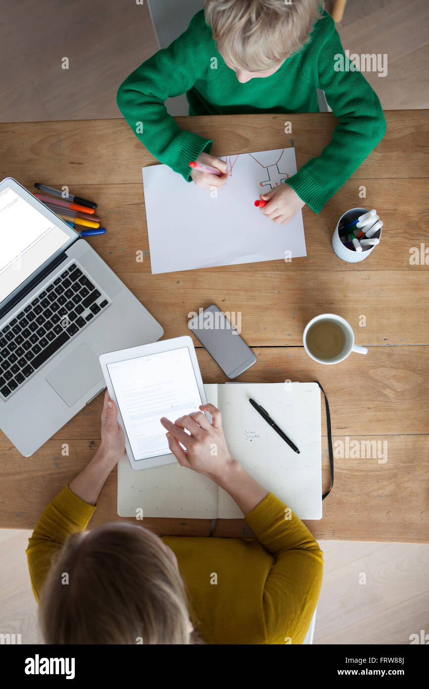 Frau am Holztisch mit digital-Tablette mit Sohn ein Bild zu malen Stockfoto