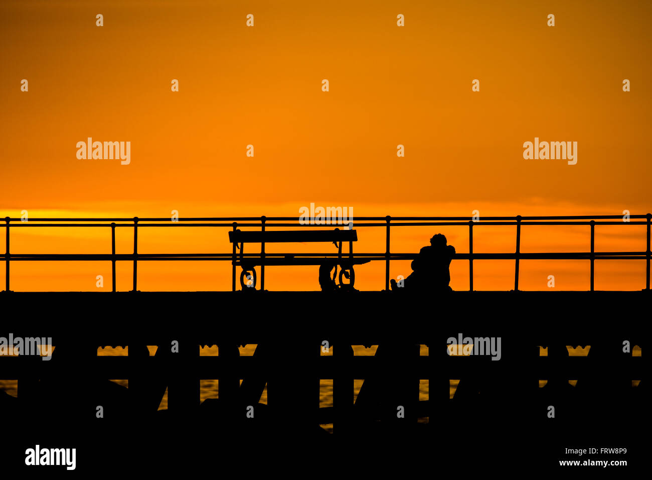 eine Person, die Geländer gelehnt, auf einem Steg den Sonnenuntergang Stockfoto