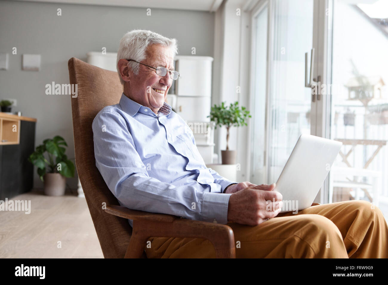 Porträt von senior Mann sitzt auf Sessel zu Hause mittels laptop Stockfoto