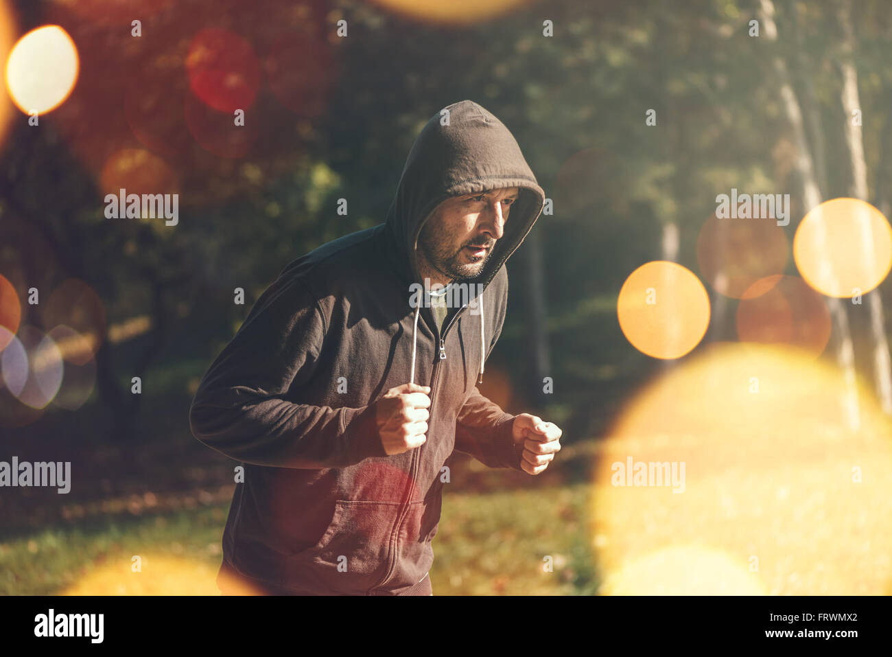 Mit Kapuze Mann Joggen im Park im frühen Herbstmorgen, gesunden Lifestyle-Konzept, Retro getönten Bild mit Tiefenschärfe Stockfoto