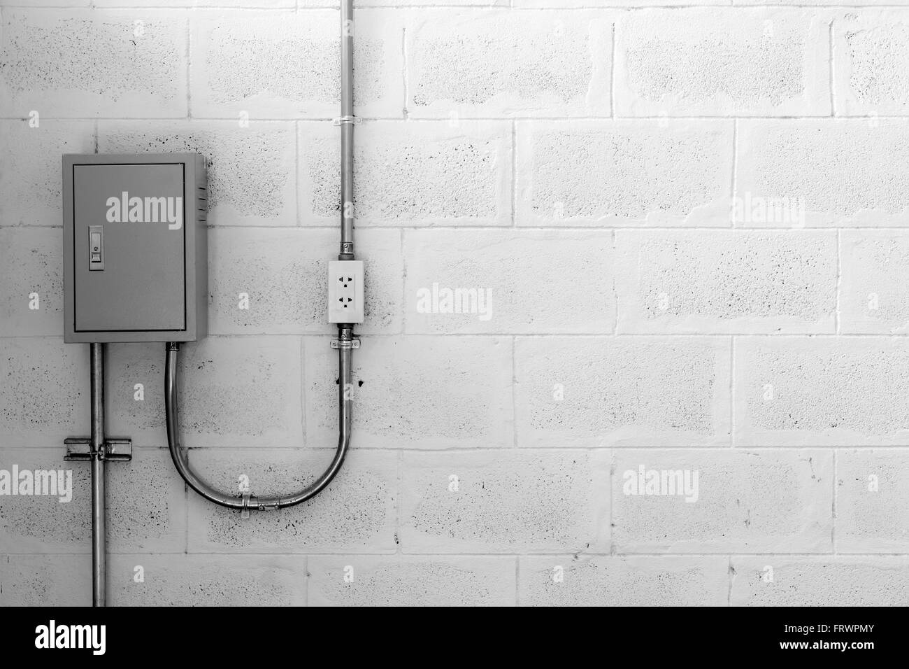 Elektrokasten auf Betonwand mit Stahlrohr und Stecker, schwarz-weiß Stockfoto