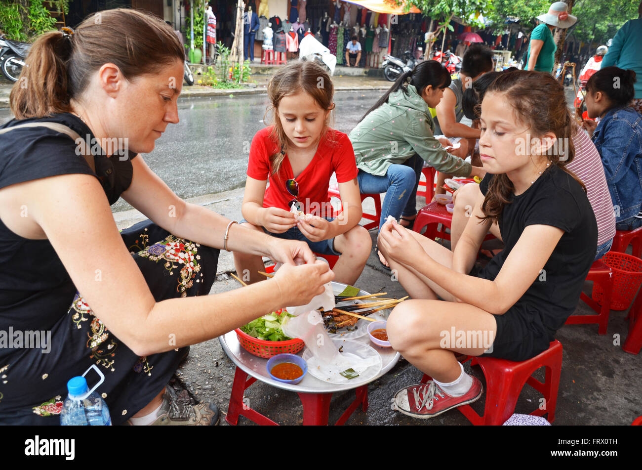 Eine Familie von Touristen isst Reis-Papier-Rollen neben einer Straße in Hoi an, Vietnam Stockfoto