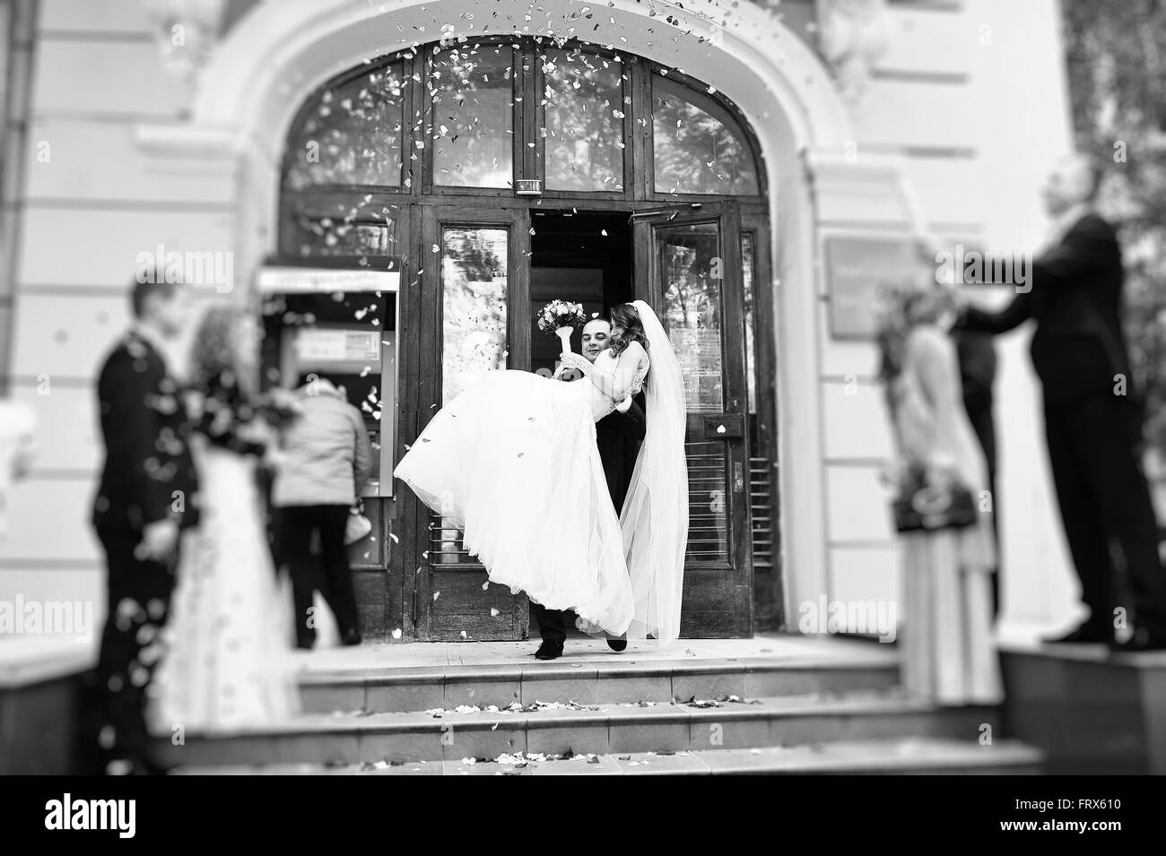 Brautpaar in Rosenblättern überschüttet wird, halten Bräutigam seine Braut auf Händen Stockfoto