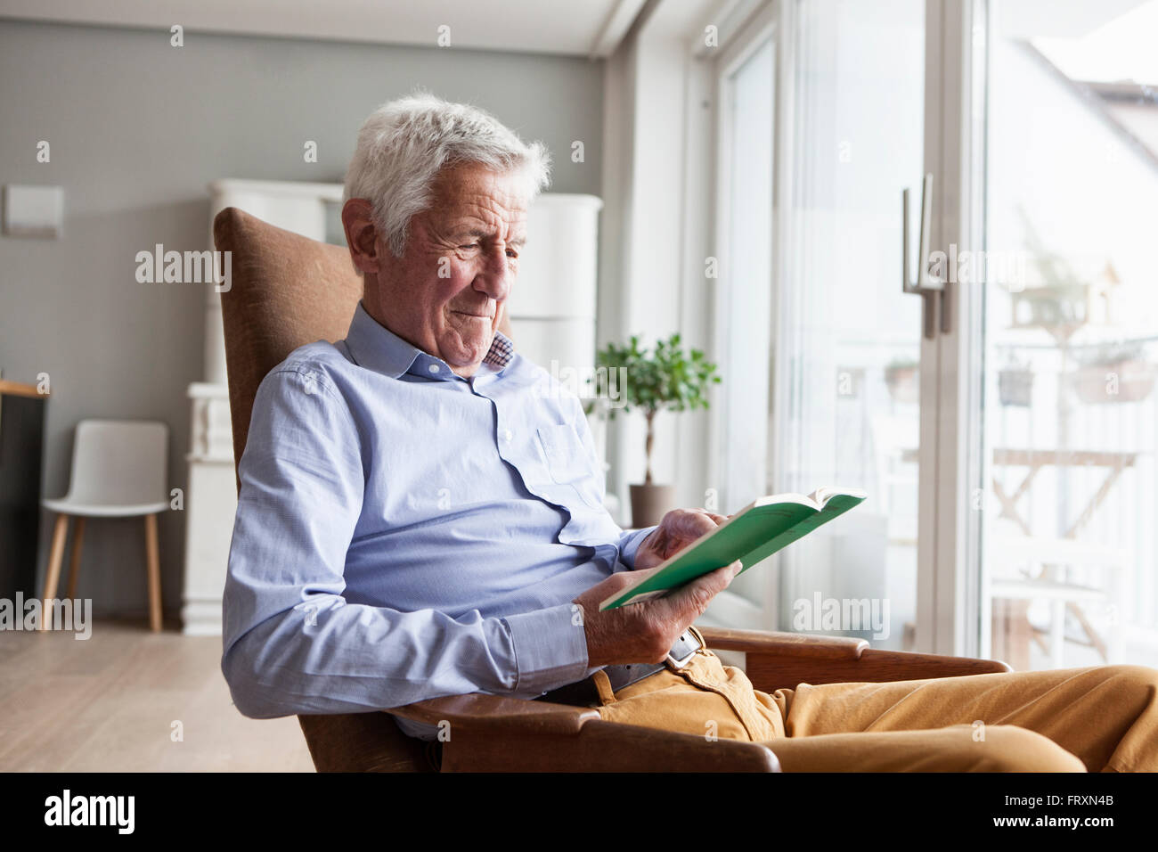 Porträt von senior Mann sitzt auf Sessel zu Hause ein Buch zu lesen Stockfoto