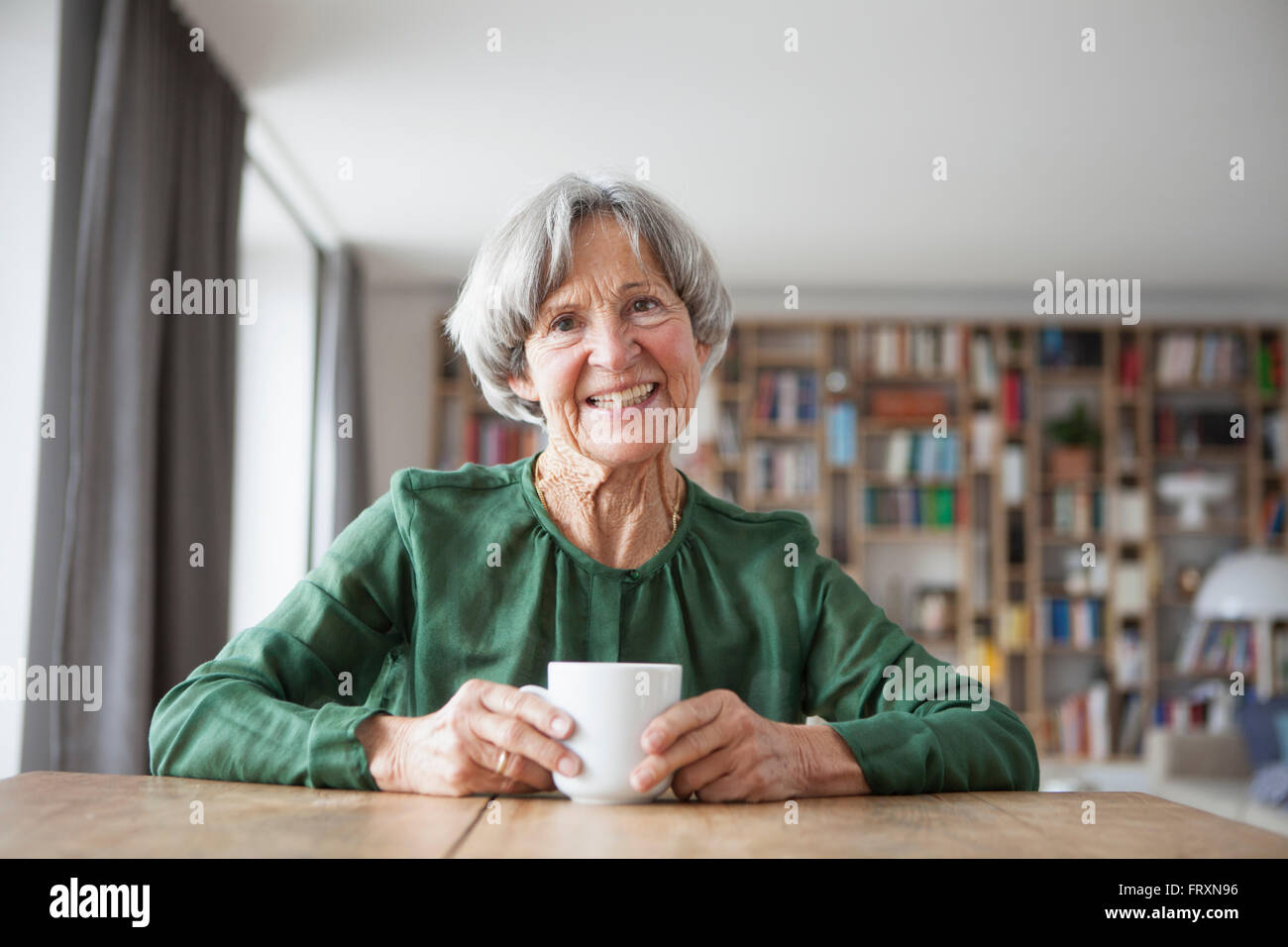 Porträt der lächelnde ältere Frau mit Tasse Kaffee am Tisch sitzen Stockfoto