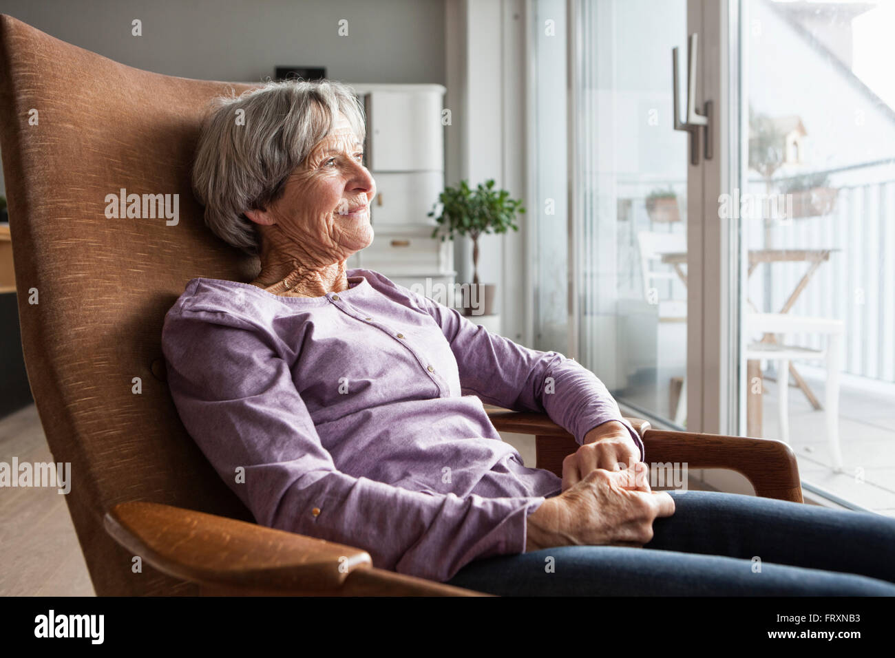 Porträt von senior Frau sitzt auf Sessel zu Hause Blick durch Fenster Stockfoto
