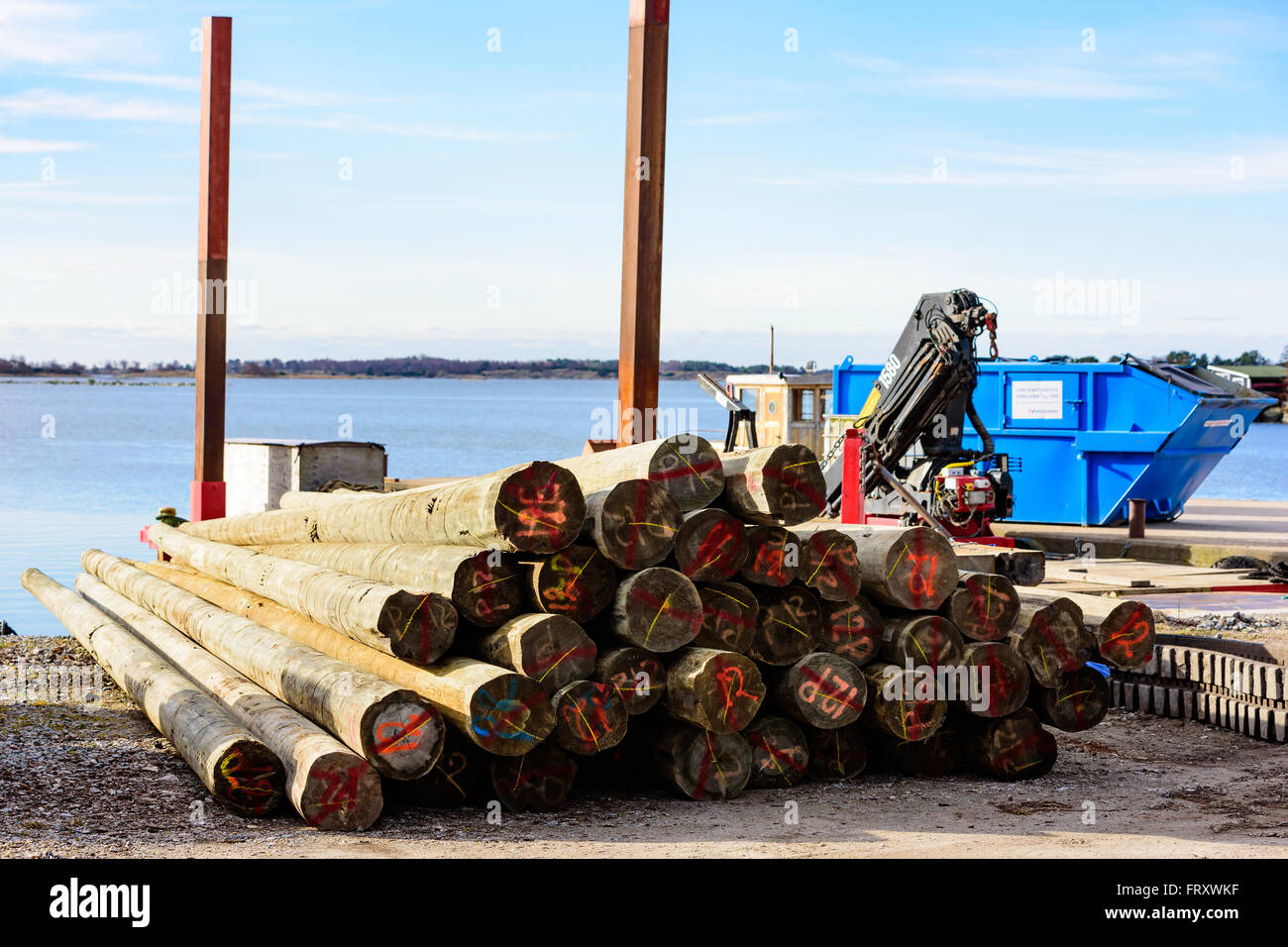Torhamn, Schweden - 18. März 2016: Ein Haufen nummerierten gefällter Stämme an der Küste. Ein Schwimmkran und eines Containers im Hintergrund. Stockfoto