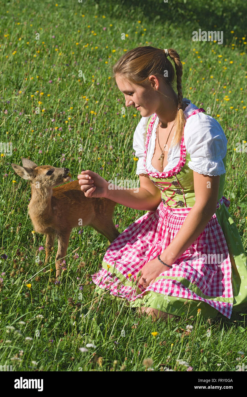 Frau im Dirndl mit zahmen Faon in einer Blumenwiese, Tirol, Österreich Stockfoto