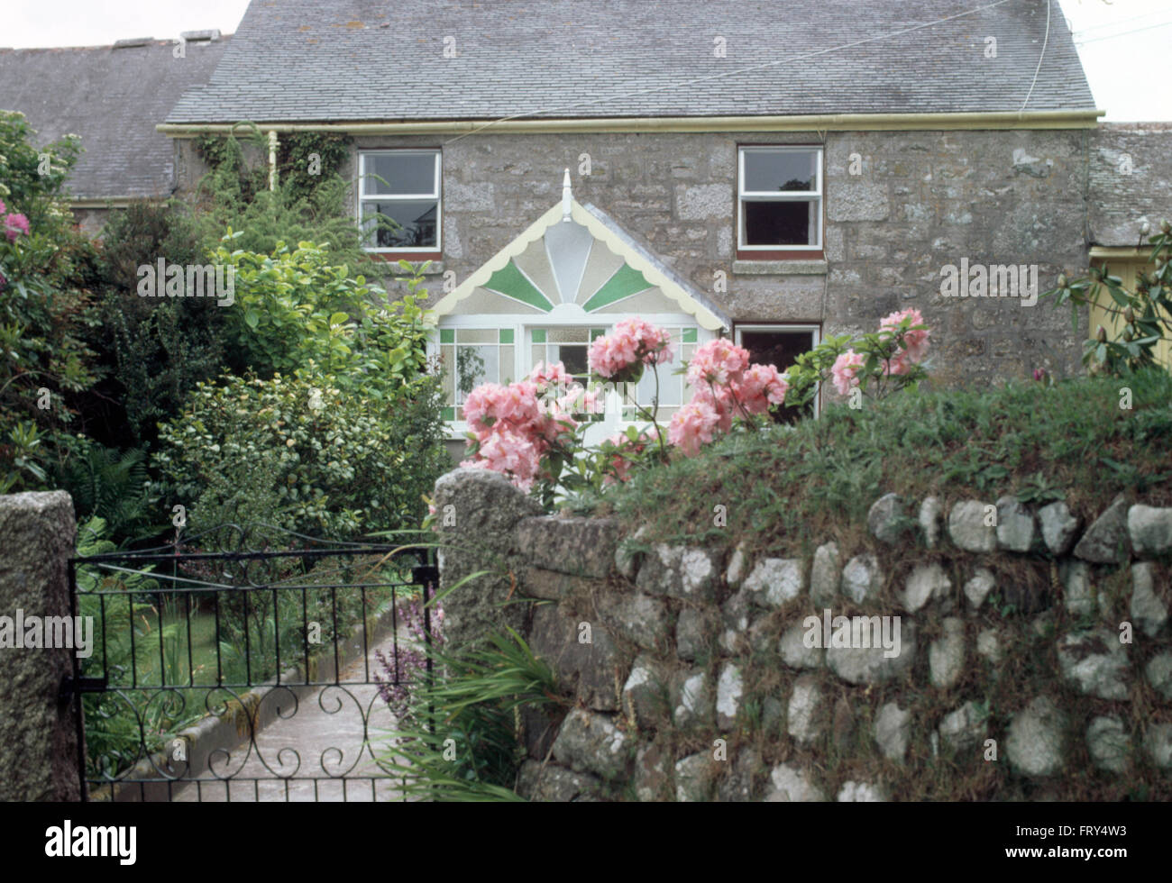 Rosa Rosen neben Wand mit schmiedeeisernen Tor vor der eine Steinhütte mit viktorianischen Glas Veranda Garten Stockfoto