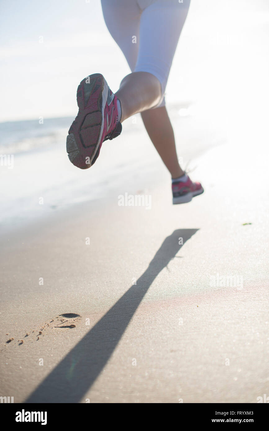 Rückansicht einer dynamischen Frau läuft am frühen Morgen verlassen Fußabdrücke im Sand am Strand Stockfoto