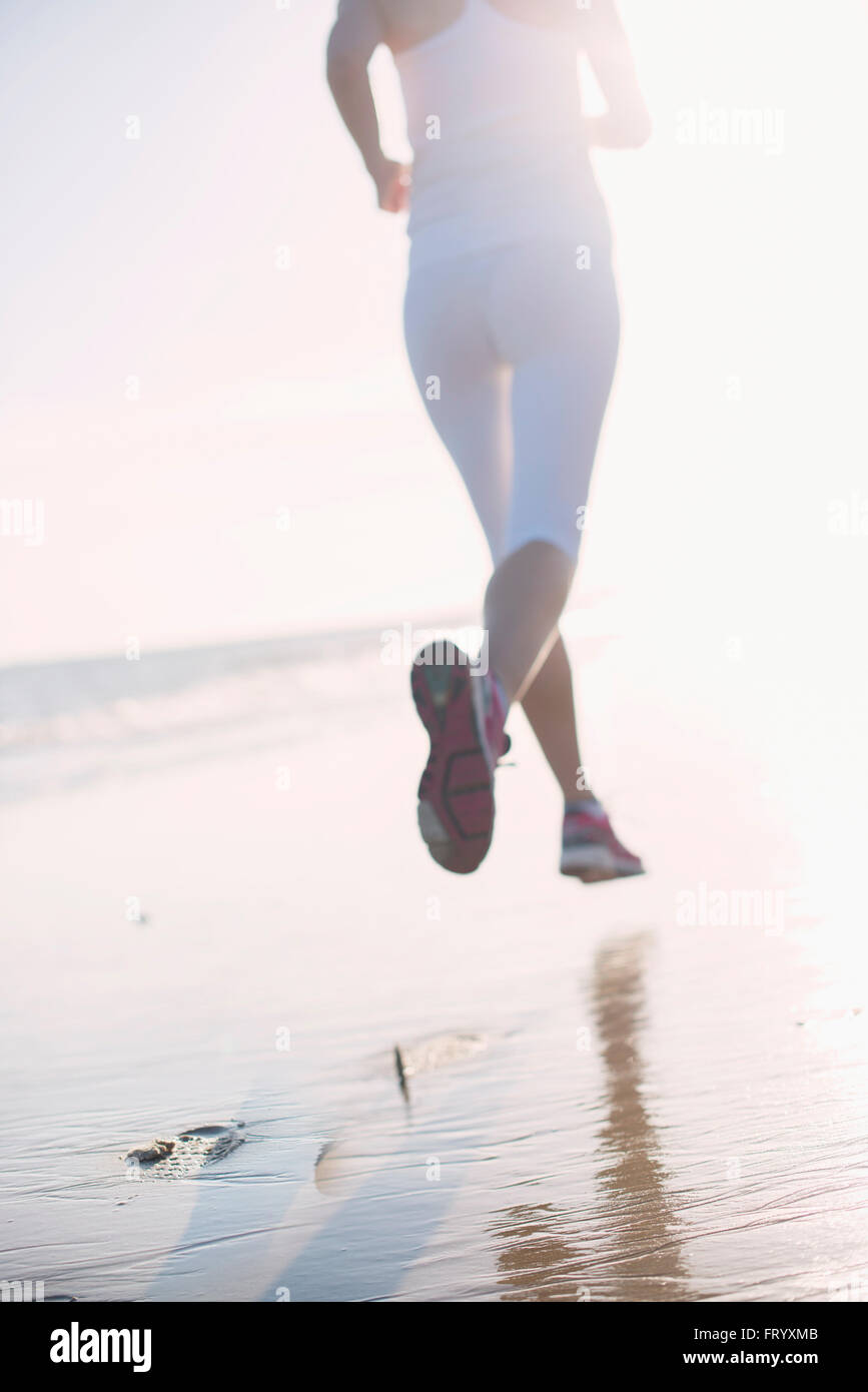 Rückansicht einer dynamischen Frau läuft am frühen Morgen verlassen Fußabdrücke im Sand am Strand Stockfoto