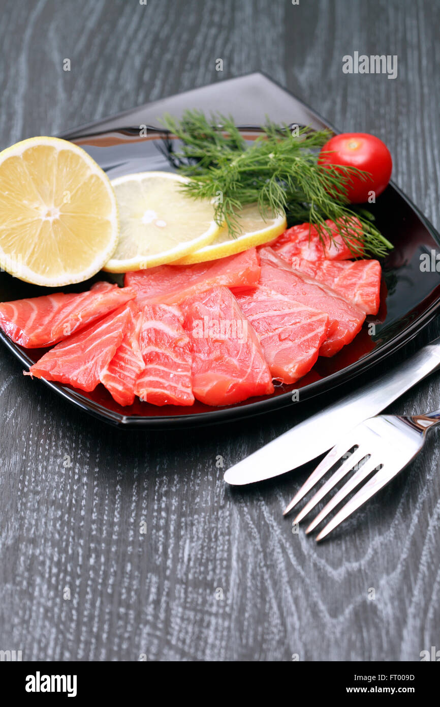 Scheiben von gesalzenen Lachs mit Zitrone auf schwarzen Druckplatte in der Nähe von Messer und Gabel Stockfoto