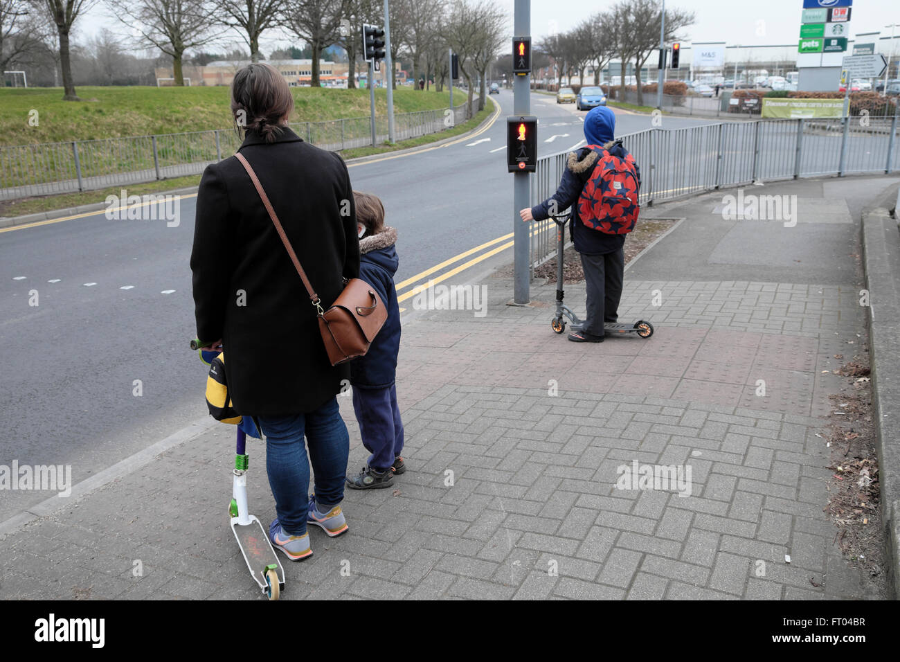 Mutter wartet an der Fußgängerüberfahrt Ampel auf die Straße mit Kindern und Roller zu Fuß zur Schule in Cardiff Wales UK KATHY DEWITT Stockfoto
