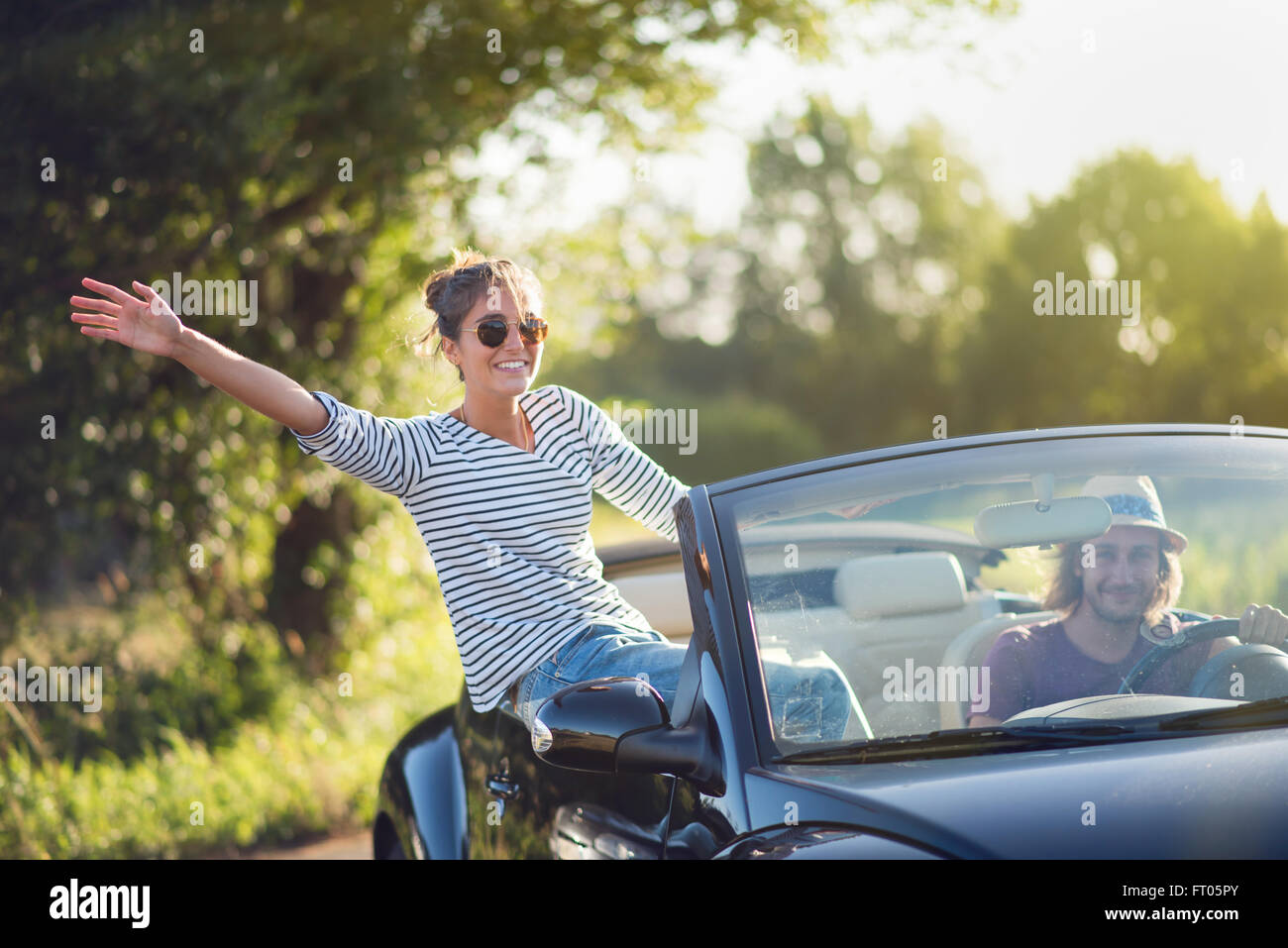 Junges Paar in seinem Cabrio, gerne im Sommer auf einer Landstraße fahren. Schuss mit Fackel Stockfoto