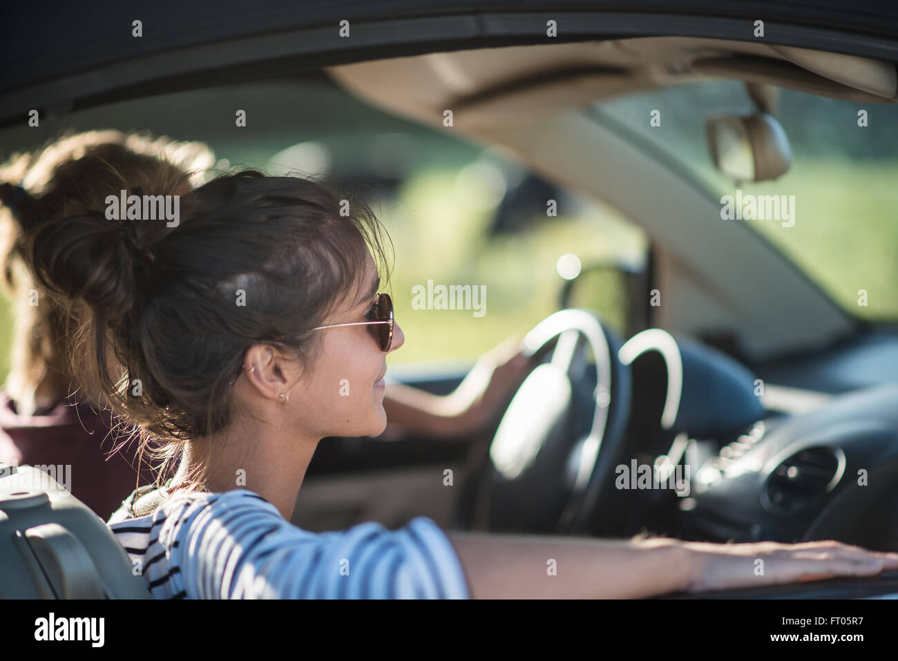 Junges Paar in seinem Wagen auf einer Landstraße fahren gerne konzentrieren sich auf die Frau. Schuss mit Fackel. Es gibt einige unscharfe Kühe im Hintergrund. Stockfoto