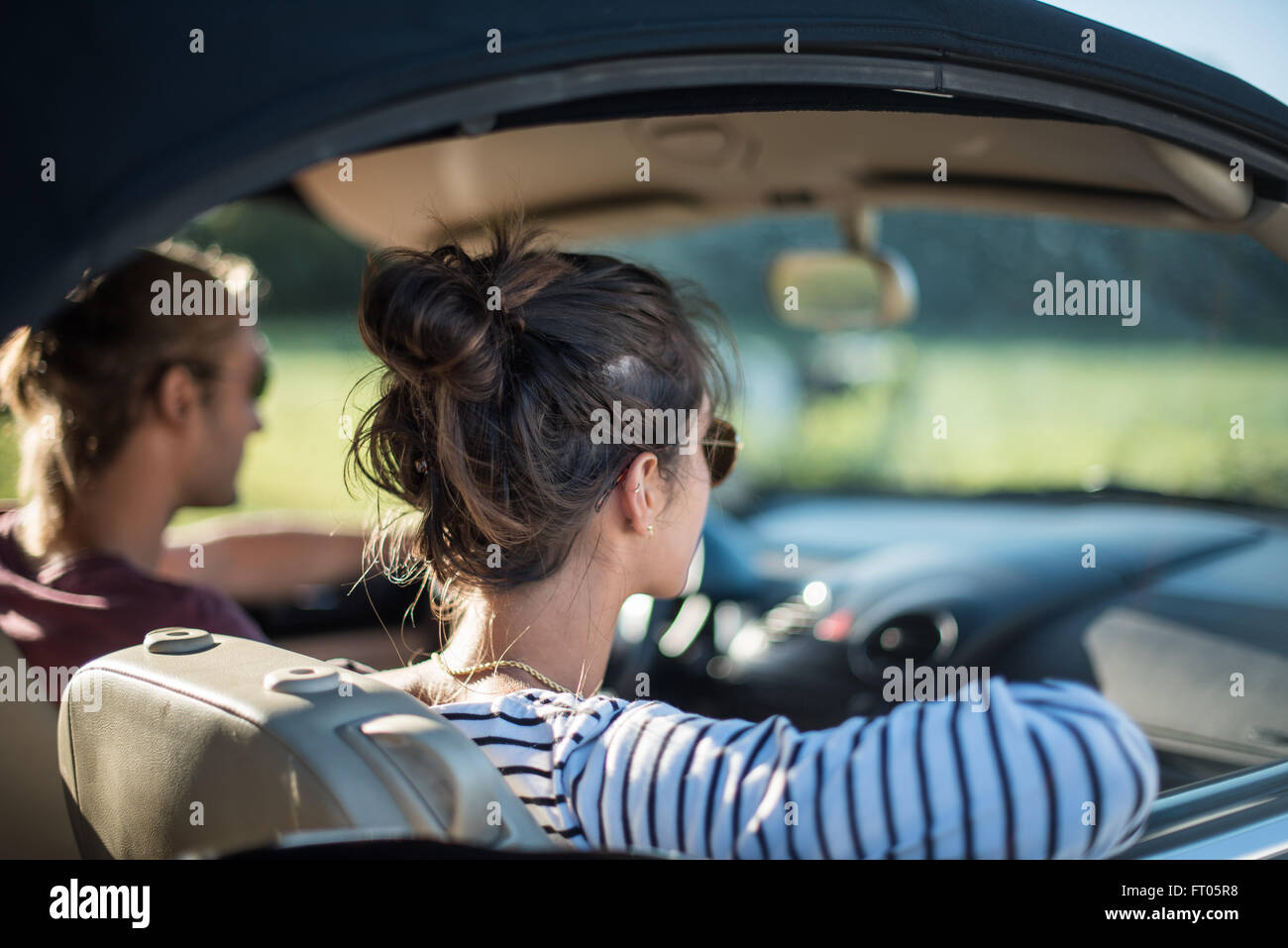 Junges Paar in seinem Wagen auf einer Landstraße fahren gerne konzentrieren sich auf die Frau. Schuss mit Fackel. Es gibt einige unscharfe Kühe im Hintergrund. Stockfoto