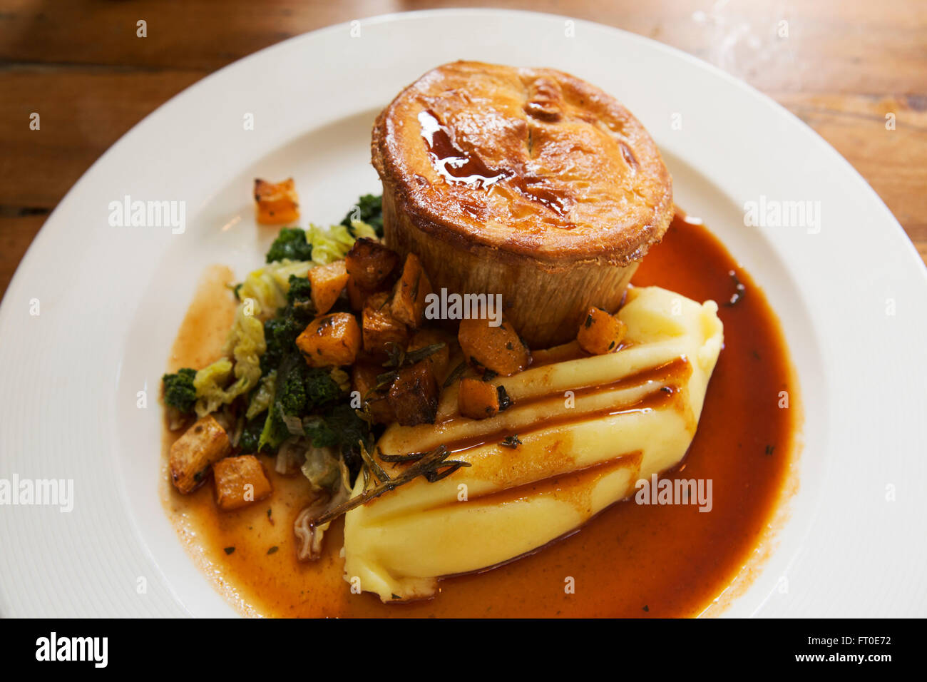 Wildbret-Kuchen serviert mit gestampften Kartoffeln und Gemüse der Saison in London, England. Das Essen wird mit einem Topf mit Soße serviert. Stockfoto
