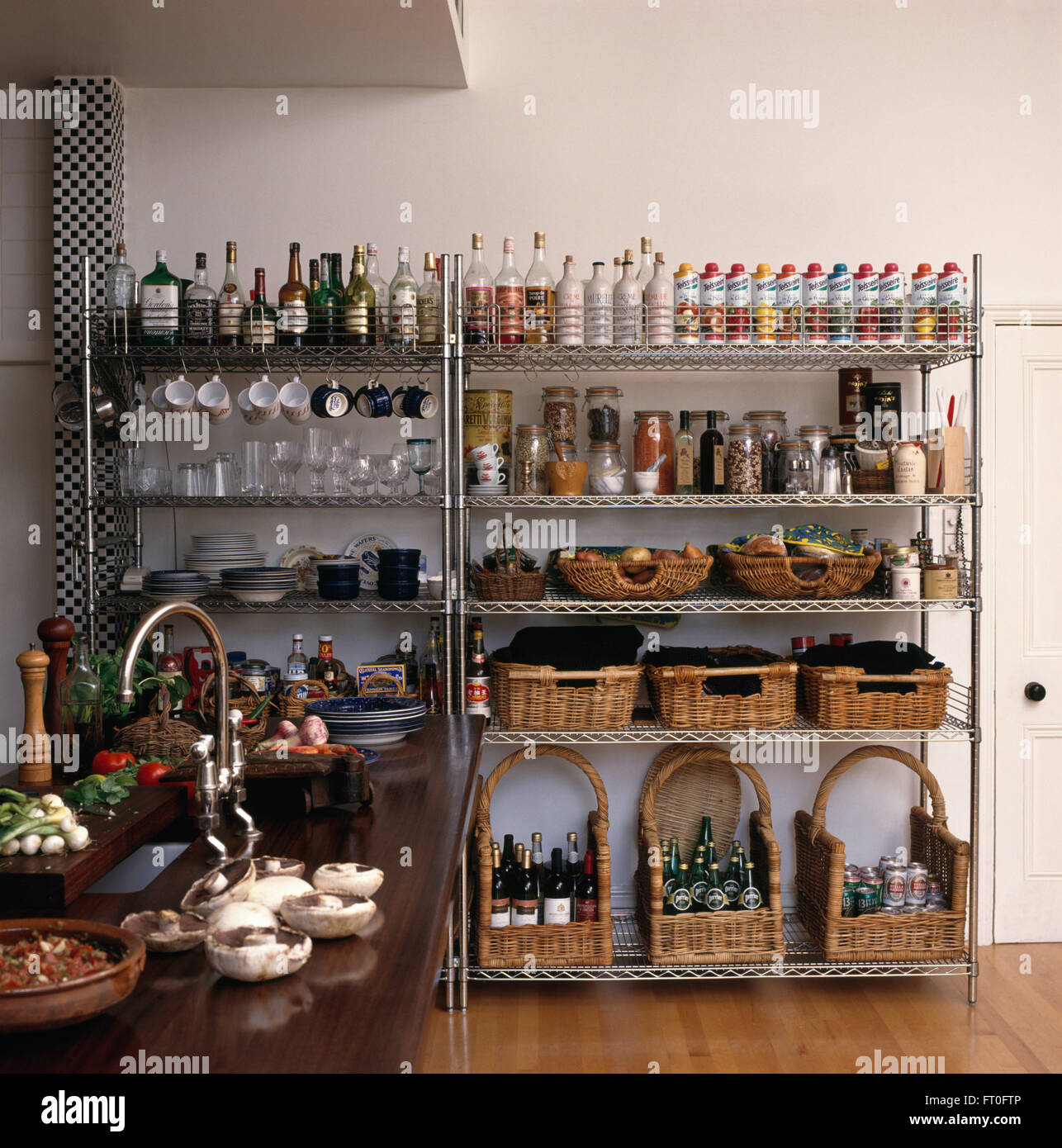 Aufbewahrung Körbe und Reihen von Flaschen auf Edelstahl Regale in modernen Küche Stockfoto