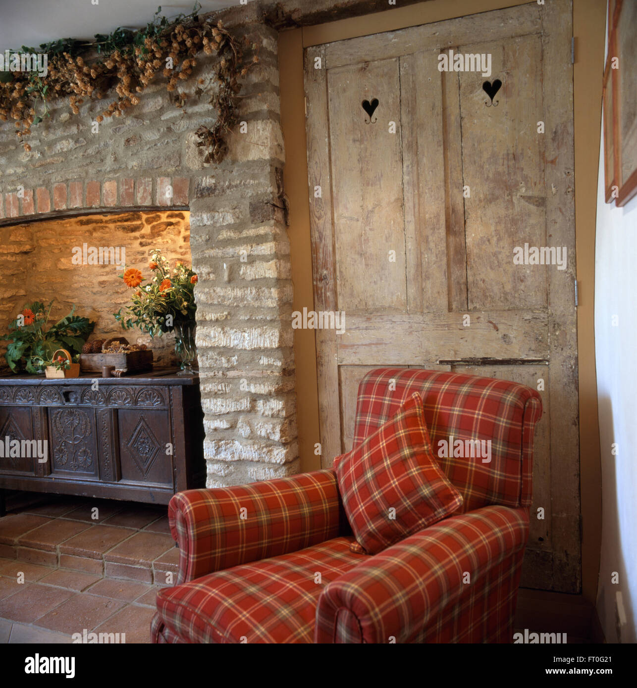 Rot aktiviert Sessel vor Kiefer Schranktüren im Wohnzimmer Land mit einer geschnitzten Eichenholz Truhe im Kamin aus Stein Stockfoto