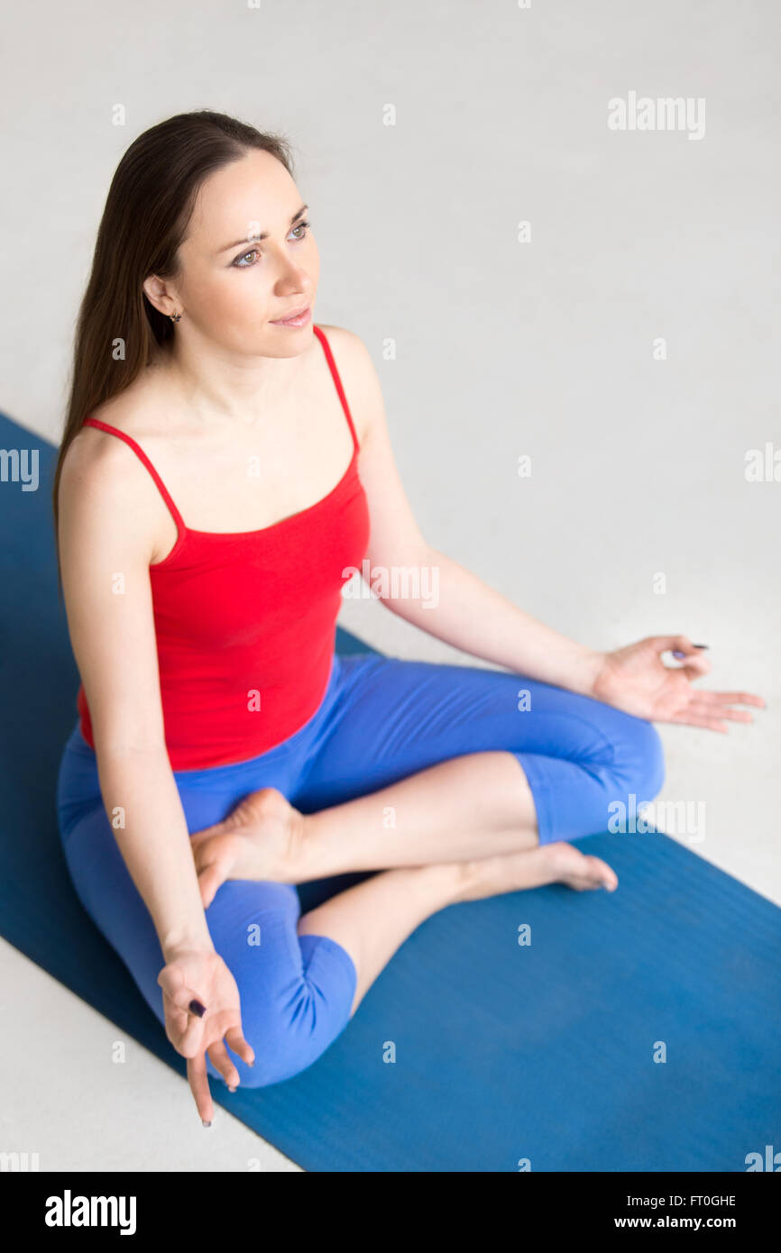 Porträt der schönen jungen Frau in leuchtend bunte Sportbekleidung arbeiten im Innenbereich auf blauen Matte. Modell auf Meditation sitzen Stockfoto