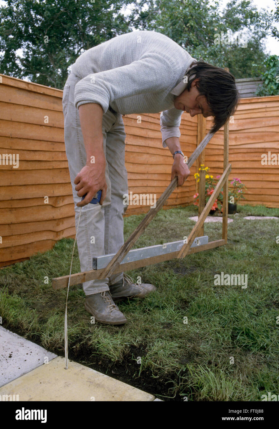 Mann mit einer Wasserwaage, um out-Bereich in einem Rasen zu messen, vor der Verlegung Pflastersteine für nur zur redaktionellen Nutzung Stockfoto