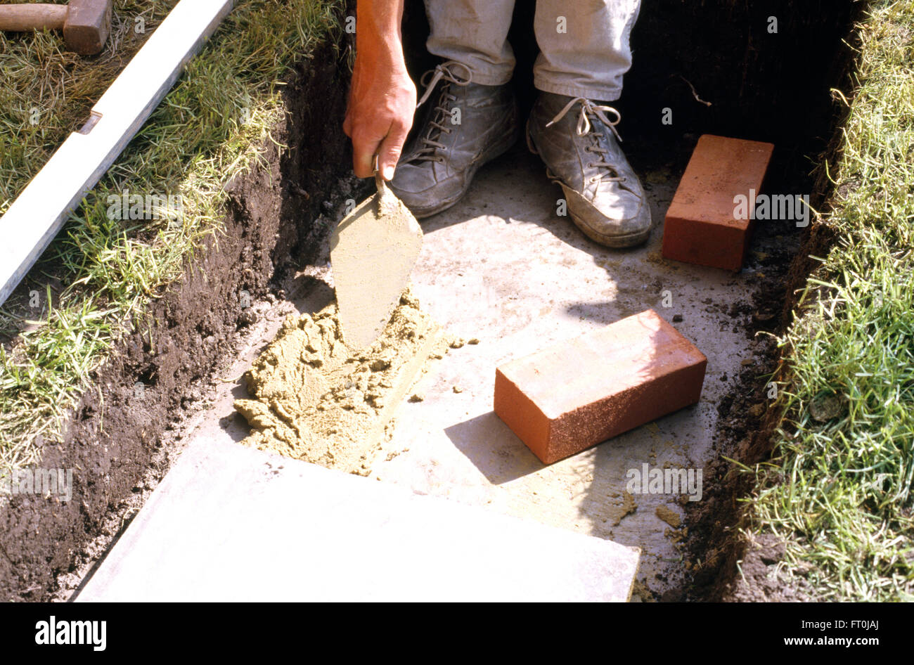 Ein Arbeiter anwenden Zement auf der Basis von einem flachen Graben in Nahaufnahme Stockfoto