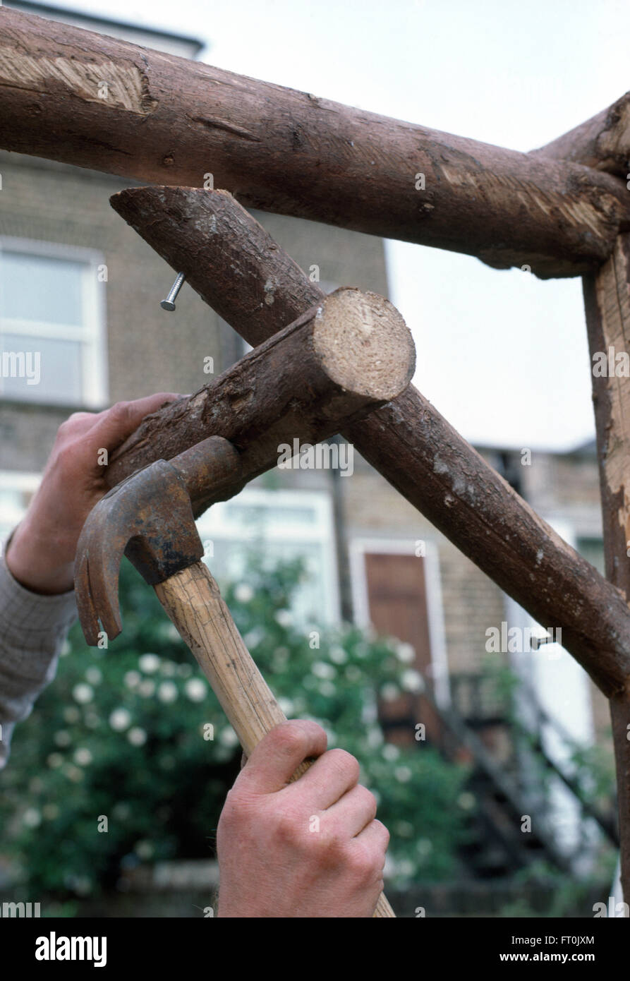 Nahaufnahme der Hand Hämmern Nägel in Holzpfosten, eine rustikale Pergola aus Holz zu machen Stockfoto