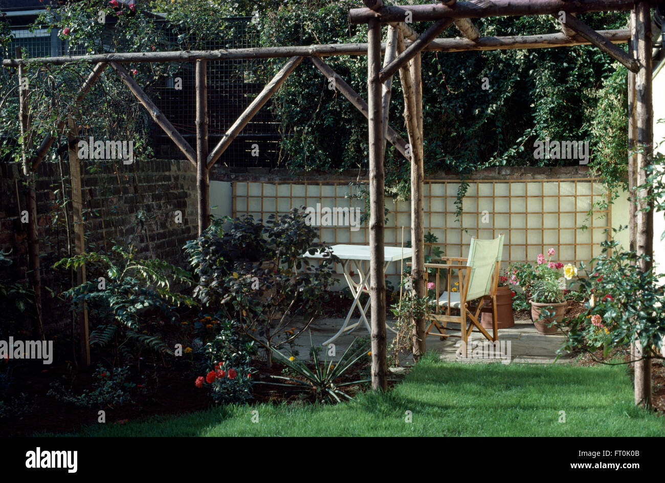 Eine rustikale Pergola aus Holz neben Terrasse mit Tisch und Regiestühle in einem neu renovierten Garten Stockfoto