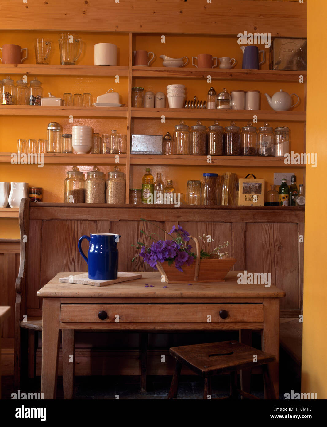 Blauer Krug auf einem kleinen Vintage Kiefer Tisch mit hölzernen Settle in orange Küche mit Glas Vorratsdosen auf einfache Kiefer Regale Stockfoto