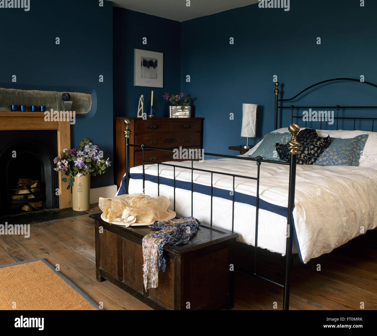 Schwarzes Schmiedeeisernes Bett mit weißen Bettdecke in einem blauen Schlafzimmer mit einem Hut auf einem Vintage Brust am Fuße des Bettes Stockfoto