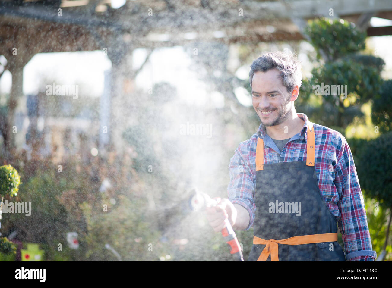 Gärtner, die Bewässerung eingemachten Bäume in einem Gartencenter