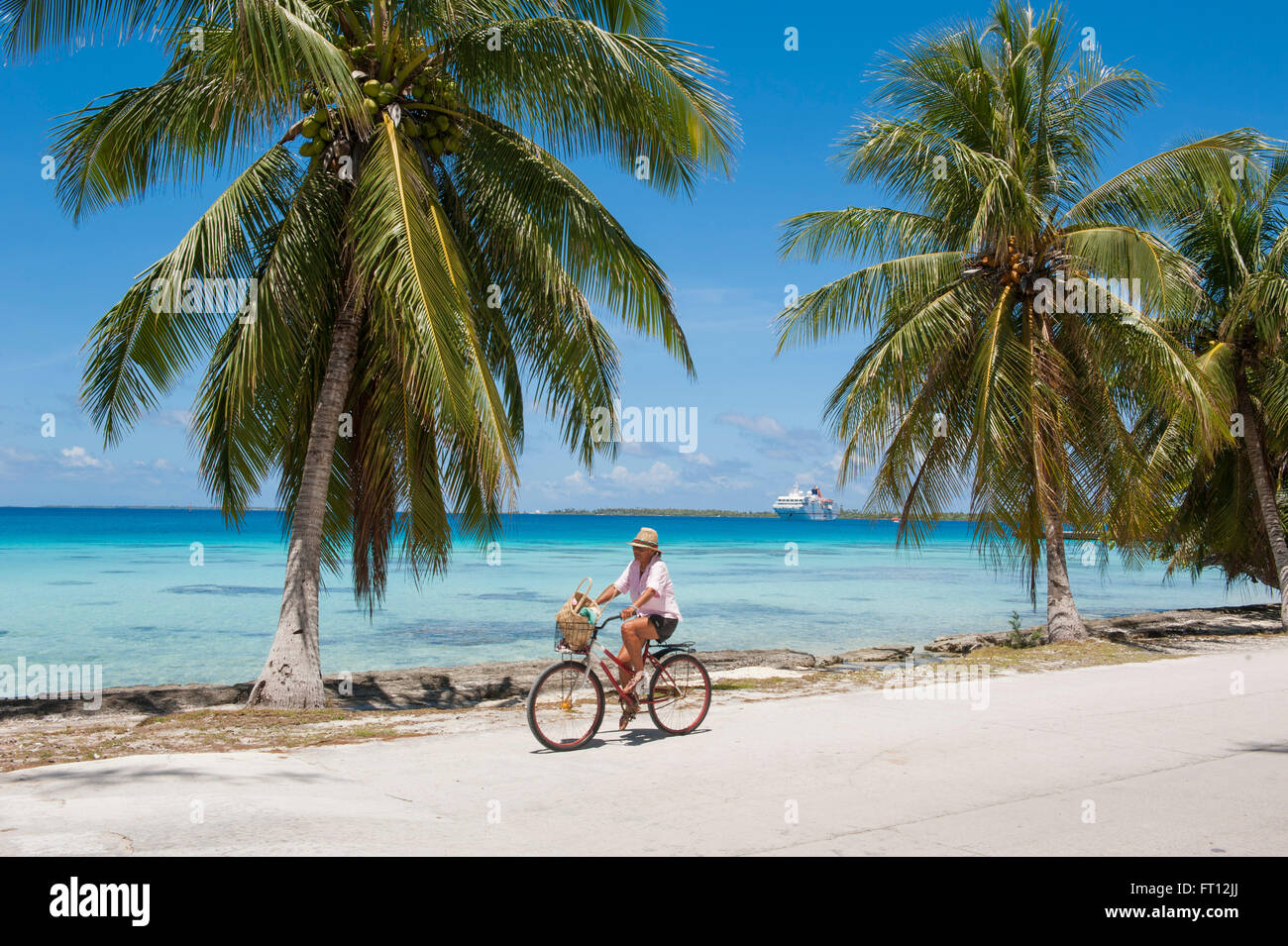 Mann mit seinem Fahrrad entlang einer Straße mit Palmen, Expedition Kreuzfahrtschiff MS Hanseatic Hapag-Lloyd Kreuzfahrten vor Anker in der Ferne, Fakarava, Tuamotu-Inseln, Französisch-Polynesien, Südsee Stockfoto