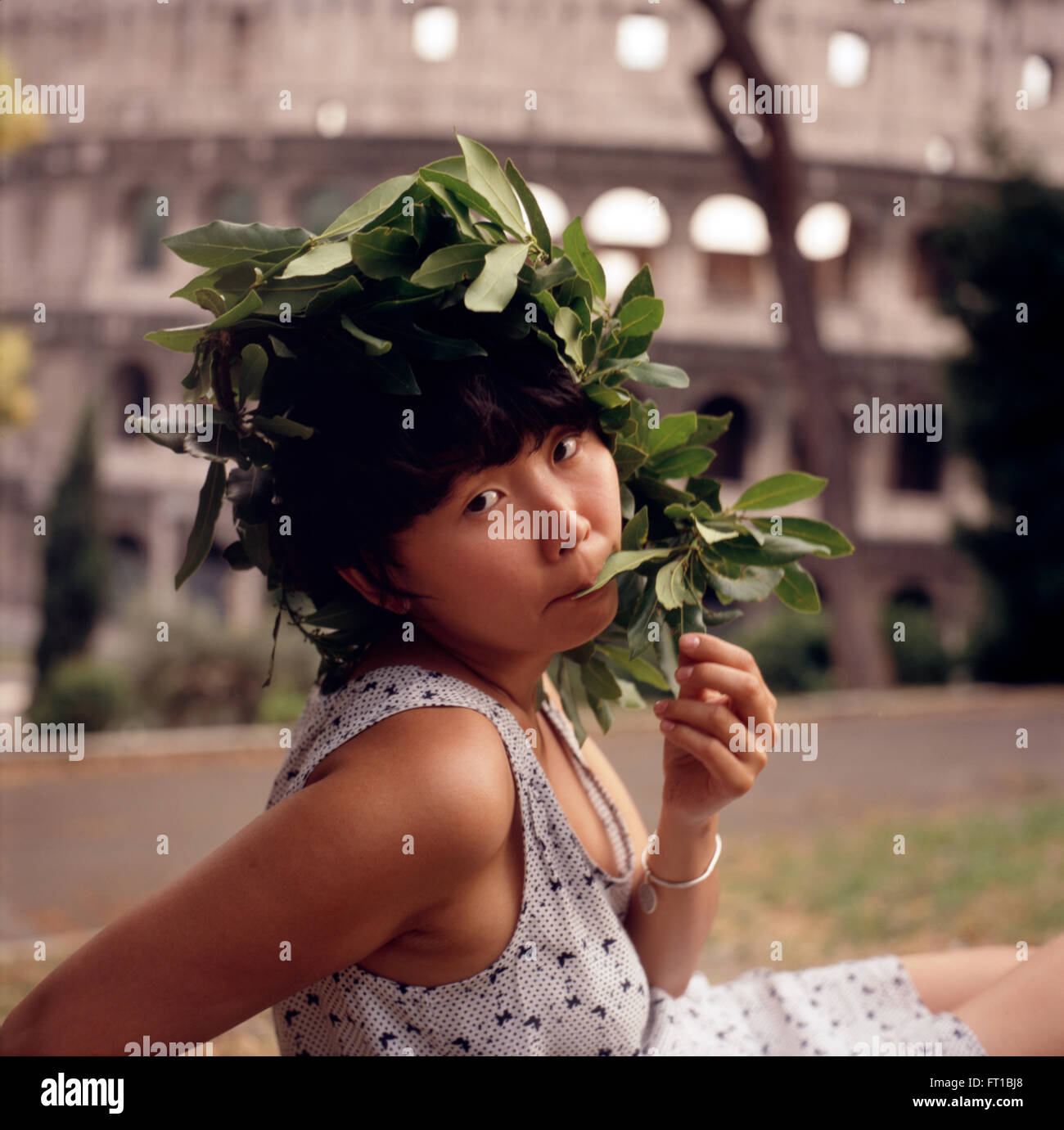 Junges asiatisches Mädchen mit Lorbeerkranz auf dem Kopf, vor dem Kolosseum, Rom, Italien Junge Frau Kranz Stockfoto
