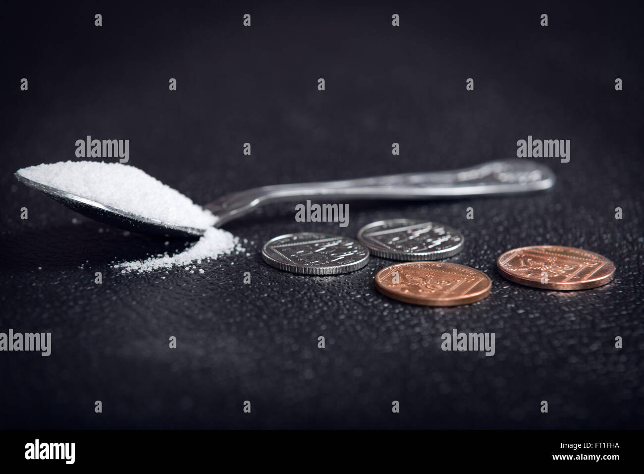 Ein Löffel Zucker bei 24 Pence auf schwarzem Hintergrund. Britische Zuckersteuer Stockfoto